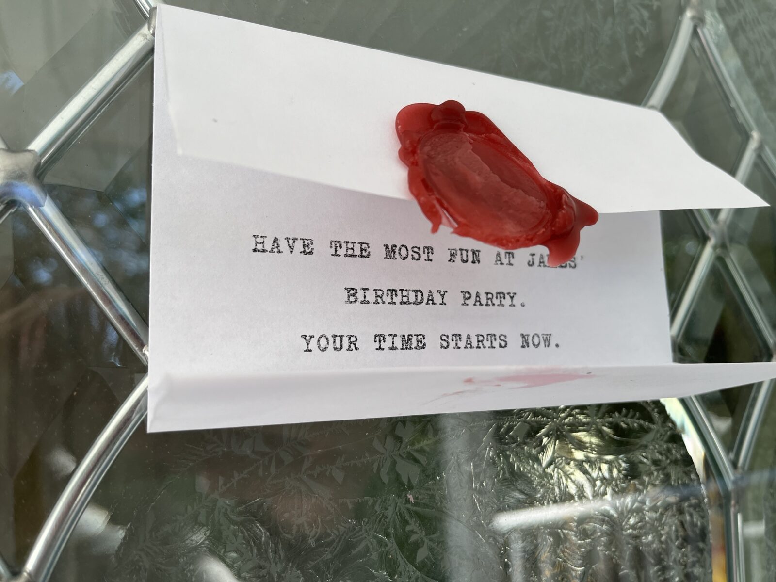 An open task card, with red wax seal, that reads “Have the most fun at James’ birthday party. Your time starts now”